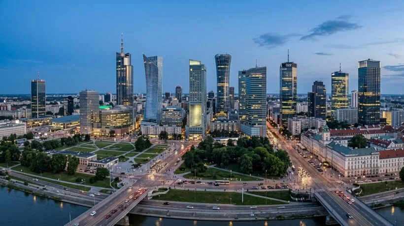Otwarty budynek warszawskiego akademika z widokiem na zielony dziedzinac i oświetlone okna pokoi studenckich.